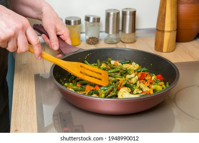 A woman cooks vegetables in a frying pan on an induction cooker