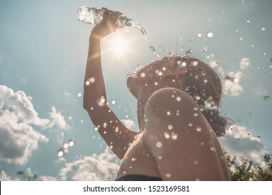 Woman Cooling Down Splashing Herself With Bottle Of Water On A Hot Sunny Day. 