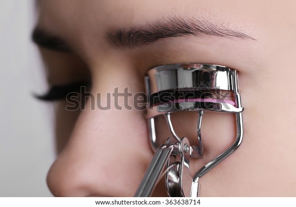 Woman
corrects eyelashes with curling tongs, close
up