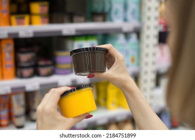 A Woman In A Cosmetics Store Holds A Jar Of Body Scrub In Her Hands. Hair Mask. Against The Background Of The Shop Window. Shopping In A Beauty Salon. Woman Testing Face Cream, Applying Body Lotion.