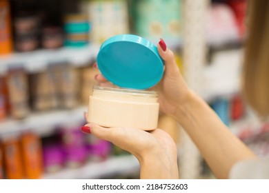 A Woman In A Cosmetics Store Holds A Jar Of Body Cream Or Hair Mask In Her Hands. A Client Buys A Shampoo Or Balm Or Hair Mask From A Cosmetics Store. The Choice Of Cosmetics In A Beauty Salon