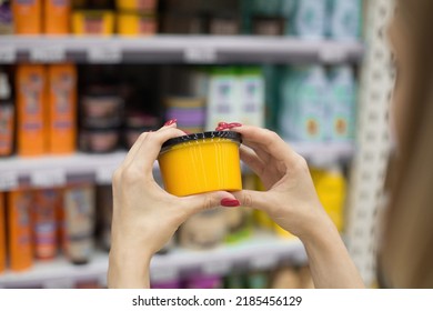 A Woman In A Cosmetics Store Holds A Jar Of Body Scrub In Her Hands. Hair Mask. Against The Background Of The Shop Window. Shopping In A Beauty Salon. Woman Testing Face Cream, Applying Body Lotion.