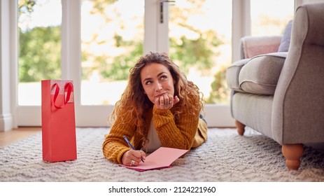 Woman In Cosy Warm Jumper Lying On Floor At Home Writing Greetings Card Or Letter