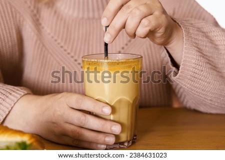 Woman in a Cosy Warm Sweater Holding a Cup of Coffee. Healthy Turmeric Autumnal Spicy Beverage. Pumpkin Latte with Curcuma in Female Hands Close up. Immunity Boosting Hot Drink of Fall Season. Cropped