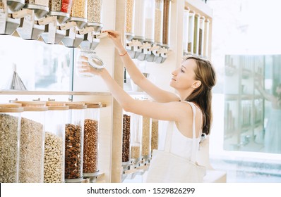 Woman with cotton bag and glass jar buying in zero waste shop. Dispensers for cereals, grains, nuts in plastic free grocery store. Sustainable shopping at small local businesses. Eco Bio Organic Food - Powered by Shutterstock