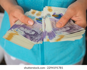 Woman counting money holding a large amount of 20 British pound notes in cash