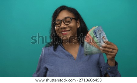 Woman counting ringgit banknotes in studio with teal background; wealth prosperity success abundance.