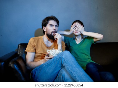 woman covered her eyes with her hands, a man with popcorn watching TV                               