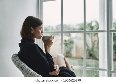 woman covered with a plaid looks out of the window at home comfort
