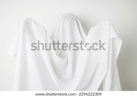 Woman is covered in a white sheet like a ghost with her hands up.