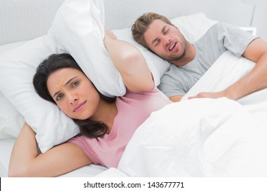 Frauen bedecken Ohren mit Kissen, während ihr Mann neben ihrem Schnarchen schnarcht