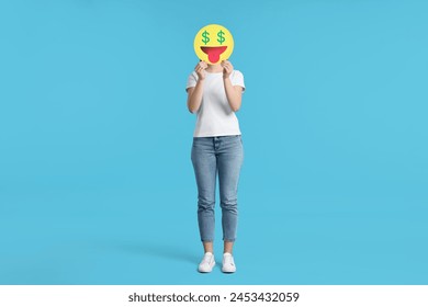 Woman covering face with dollar signs instead of eyes on light blue background - Powered by Shutterstock