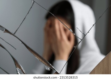 Woman covering face with hands near broken mirror. Mental problems