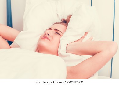 Woman covering her ears with pillow. She is stressed and sleepless. Insomnia.