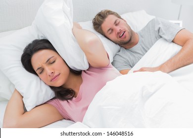 Frau bedeckt ihre Ohren mit Kissen, während ihr Mann neben ihrem Schnarchen schnarcht
