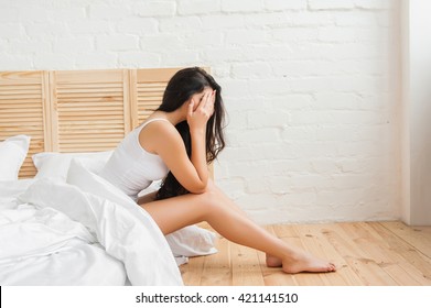 woman covering her face with hands while sitting in bed