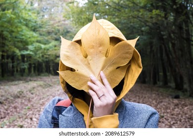 A woman is covering her face with a large yellow leaf. The symbol of autumn is colorful leaves. Selective focus.