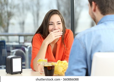 Woman covering her mouth to hide smile or bad breath during a date in a coffee shop with a window in the background