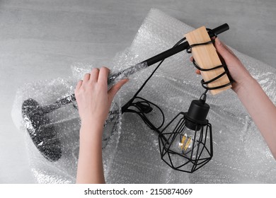 Woman covering lamp with bubble wrap at light grey table, closeup