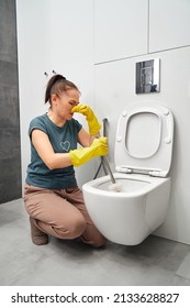 Woman Covering Nose To Avoid Bad Smell While Cleaning A Smelly Toilet Bowl.