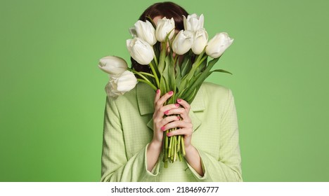 Woman covers her face with bouquet of tulips. Girl smells flowers in her hands, standing over green background
