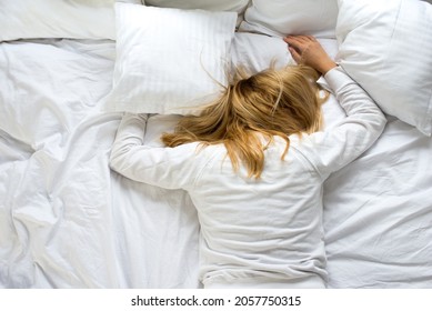 A woman covers her face with a pillow. The woman lies tired on a white bed. Oversleep, not getting enough sleep concept. Young beautiful blonde woman lying in bed. Early wake up concept - Powered by Shutterstock