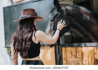 A woman in a cowboy hat gently petting a horse in a stable, highlighting the bond and affection between humans and animals. - Powered by Shutterstock