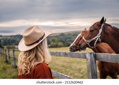 Woman with cowboy hat looking at her horses on pasture. Cowgirl in animal farm - Powered by Shutterstock