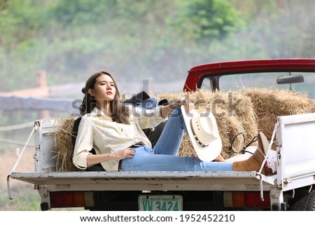 A woman in a cowgirl style sits in a horse ranch with a western farm environment.