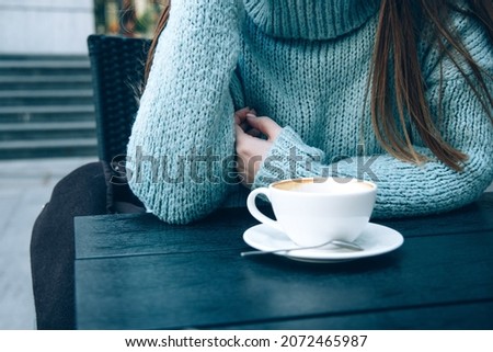 Woman in a cozy blue sweater drinking coffee in a street cafe. Cup of morning coffee. Noface