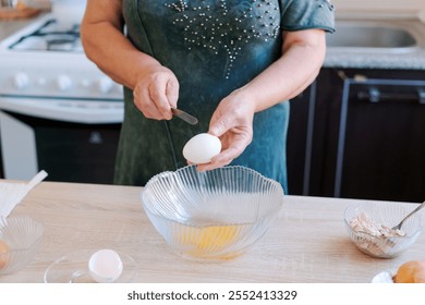 Woman is cracking an egg into a bowl on a wooden table. She is wearing a green dress - Powered by Shutterstock