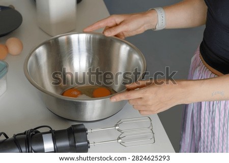 Woman cracking fresh eggs and adding sugar into stainless steel bowl on kitchen counter horizontal. Step-by-step recipe photo perfect for cooking blogs, breakfast branding and food editorial content. 