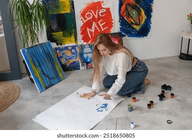 Woman Creates Blue Handprint Artwork on large white canvas in Studio laying on the floor - Powered by Shutterstock