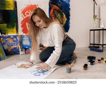 Woman Creates Blue Handprint Artwork on large white canvas in Studio laying on the floor - Powered by Shutterstock