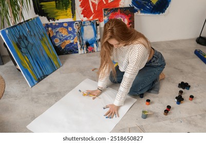 Woman Creates Blue Handprint Artwork on large white canvas in Studio laying on the floor - Powered by Shutterstock