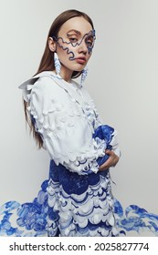 Woman in creative dress with blue and white waves and wire mask. Drawing and ruffles on clothes. Model standing on the blue waves drawing                                                  