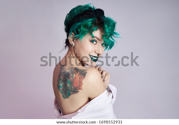 Woman with creative green\
coloring hair and makeup, toxic strands of hair. Bright color curly\
hair on the girl head, professional makeup. Woman with\
tattoo