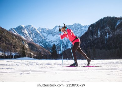 Woman cross country skiing on snowy flat terrain, at the foothill of beautiful mountain peaks, wide shot.