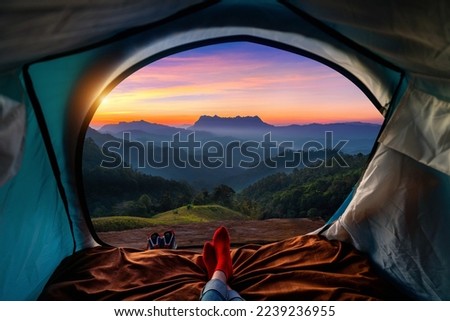 Woman cross leg on blanket in camping tent with sleeping bags on mountain hill. view from inside with Doi luang chiang dao mountains.