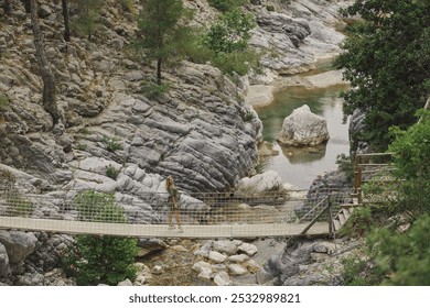 A woman crosses a suspension bridge over a rocky river in Goynuk Canyon, set in a natural, rugged landscape. Perfect for promoting hiking, eco-tourism, and adventure travel destinations.  - Powered by Shutterstock