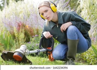 Woman Crouching Down By Garden Strimmer