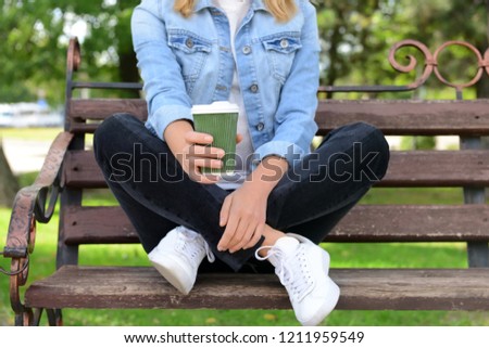 Woman with cup of aromatic coffee sitting on bench in park