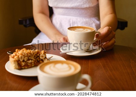 A woman with a cup of aromatic coffee and a sweet nut cake sits in a cafe or restaurant. The girl drinks a hot latte or cappuccino after breakfast with a delicious dessert