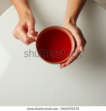 Woman with cup of black tea at white table indoors, top view