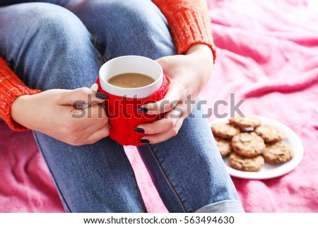Woman with cup of coffee sitting on pink plaid