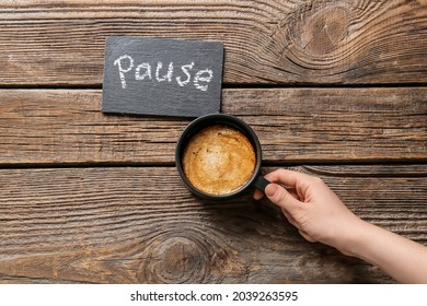 Woman with cup of coffee and word PAUSE on wooden background
