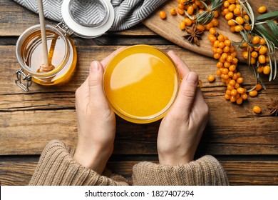 Woman with cup of fresh sea buckthorn tea at wooden table, top view
