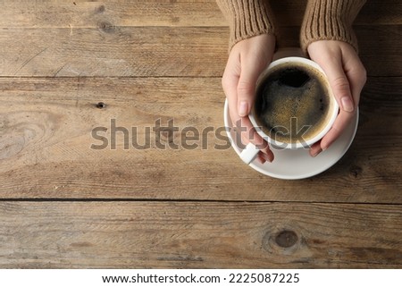 Woman with cup of hot aromatic coffee at wooden table, top view. Space for text