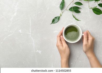 Woman with cup of matcha tea and leaves at table, top view