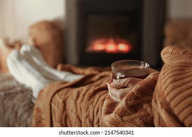 Woman with cup of tea resting near fireplace at home, closeup - Powered by Shutterstock